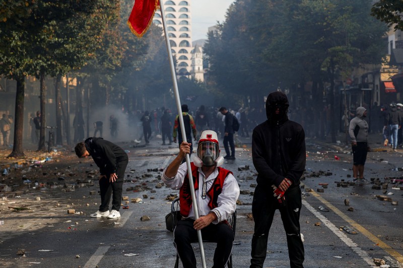 Orang-orang berkumpul di dekat api sementara gumpalan asap hitam membubung, di tengah aksi protes anti-pemerintah oleh para mahasiswa, di Tirana, Albania, 14 Oktober 2026. (REUTERS/Florion Goga)