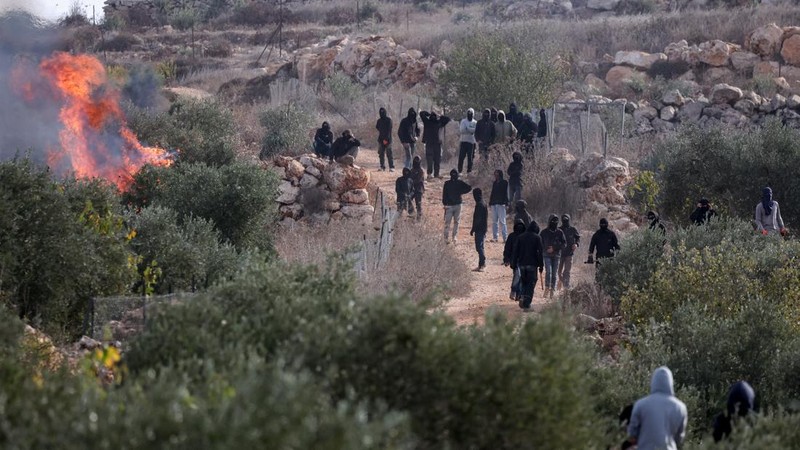 Warga Palestina memandang ke arah para pemukim Israel yang berdiri di dekat api di tengah bentrokan saat musim panen zaitun di Abu Falah, dekat Ramallah, di Tepi Barat yang diduduki Israel, 16 Oktober 2026.
