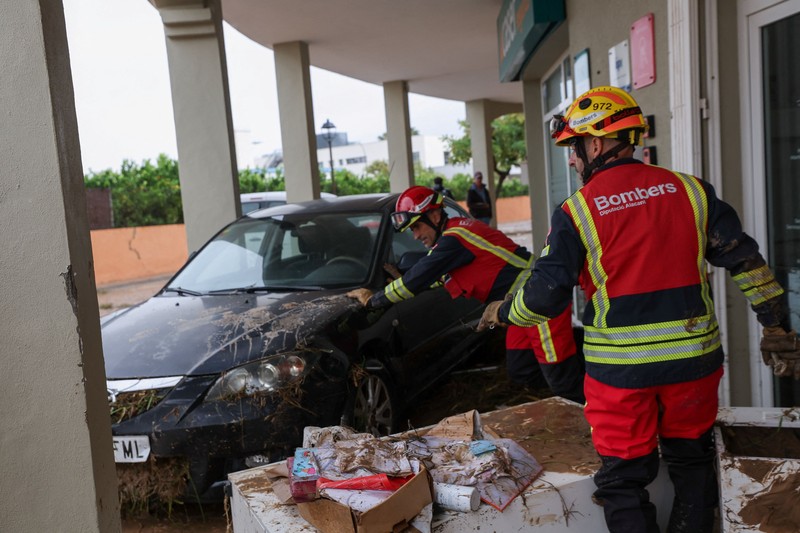 Firefighters work to remove a car on top of other objects in a mud-covered street, following torrential rains, which caused floods in eastern Spain, in Els Poblets, Alicante province, Spain, October 19, 2026. REUTERS/Eva Manez