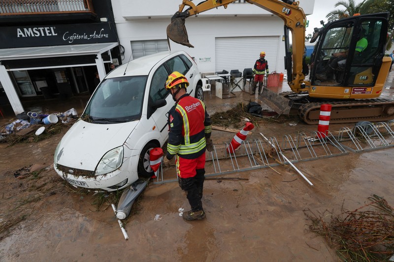 Firefighters work to remove a car on top of other objects in a mud-covered street, following torrential rains, which caused floods in eastern Spain, in Els Poblets, Alicante province, Spain, October 19, 2026. REUTERS/Eva Manez