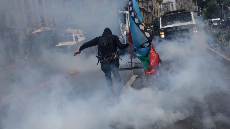 Seorang pengunjuk rasa berjalan di tengah gas air mata pada hari digelarnya aksi massa untuk memperingati tujuh tahun protes dan kerusuhan tahun 2019, di Santiago, Chili, 18 Oktober 2026. (REUTERS/Pablo Sanhueza)
