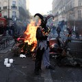Seorang pengunjuk rasa yang mengenakan kostum berdiri di depan kobaran api, di Paris, Prancis, 18 Oktober 2026. (REUTERS/Abdul Saboor)