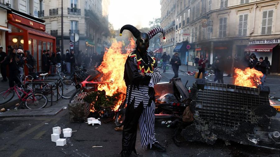 Seorang pengunjuk rasa yang mengenakan kostum berdiri di depan kobaran api, di Paris, Prancis, 18 Oktober 2026.