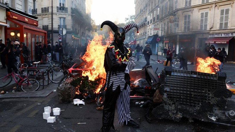 Seorang pengunjuk rasa yang mengenakan kostum berdiri di depan kobaran api, di Paris, Prancis, 18 Oktober 2026.