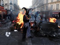 Seorang pengunjuk rasa yang mengenakan kostum berdiri di depan kobaran api, di Paris, Prancis, 18 Oktober 2026. (REUTERS/Abdul Saboor)