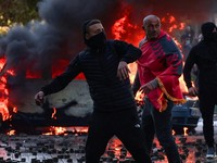 Seorang pengunjuk rasa yang menyelimuti dirinya dengan bendera nasional Albania tampak mengamati saat massa terlibat bentrokan dengan polisi dalam sebuah aksi protes anti-pemerintah yang digelar oleh para mahasiswa di Tirana, Albania, pada 17 Oktober