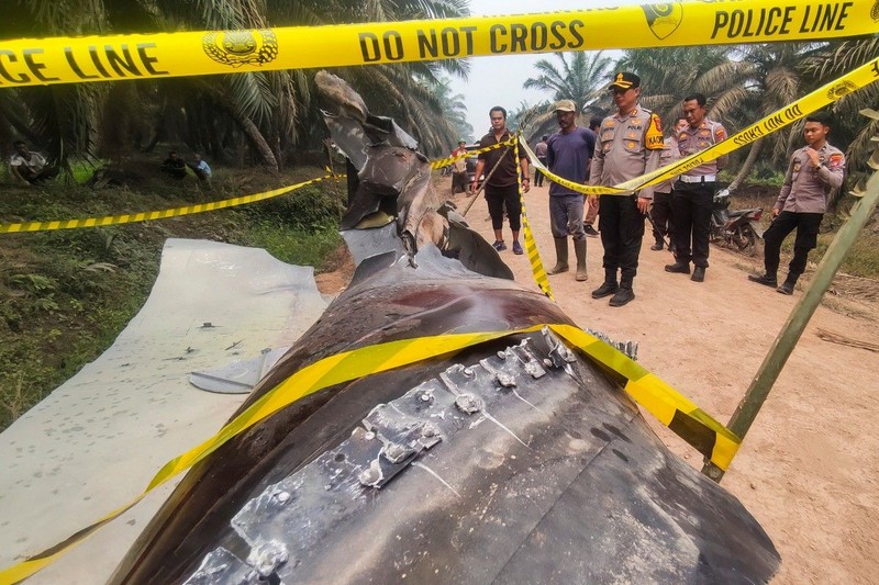 This picture taken on October 19, 2026 shows Indonesian police officers inspecting a large charred metallic fragment, suspected to be rocket debris, at an oil palm plantation in East Kotawaringin Regency, in Indonesia's Central Kalimantan province. Indonesian authorities were investigating October 20 after a piece of rocket the size of a car crashed into an oil palm plantation on Indonesian Borneo. (Photo by AHMAD SYIHAB / AFP)