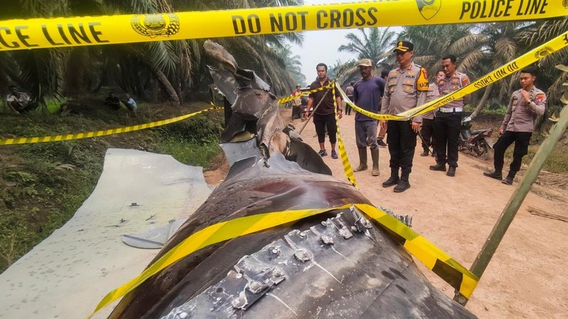 This picture taken on October 19, 2026 shows Indonesian police officers inspecting a large charred metallic fragment, suspected to be rocket debris, at an oil palm plantation in East Kotawaringin Regency, in Indonesia's Central Kalimantan province. I