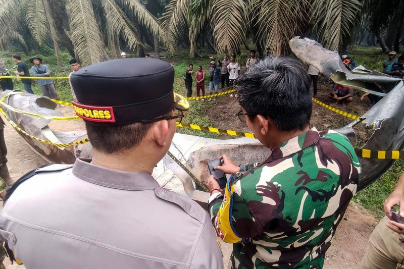 This picture taken on October 19, 2026 shows Indonesian police officers inspecting a large charred metallic fragment, suspected to be rocket debris, at an oil palm plantation in East Kotawaringin Regency, in Indonesia's Central Kalimantan province. Indonesian authorities were investigating October 20 after a piece of rocket the size of a car crashed into an oil palm plantation on Indonesian Borneo. (Photo by AHMAD SYIHAB / AFP)