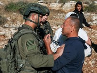 Seorang pria Palestina berbicara dengan pasukan Israel saat mereka menahan pria Palestina lainnya di tengah musim panen zaitun di kebun zaitun milik warga Palestina di Deir Abu Mashal, dekat Ramallah, di Tepi Barat yang diduduki Israel, pada 19 Oktob