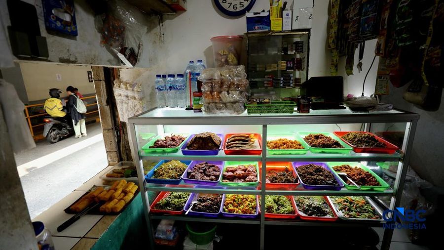 Pekerja membeli makanan dan minuman melalui lubang kecil di tembok pembatas kawasan permukiman dan pusat perbelanjaan di kawasan Kemang, Jakarta, Rabu (21/10/2026).