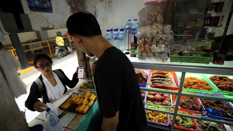 Pekerja membeli makanan dan minuman melalui lubang kecil di tembok pembatas kawasan permukiman dan pusat perbelanjaan di kawasan Kemang, Jakarta, Rabu (21/10/2026).
