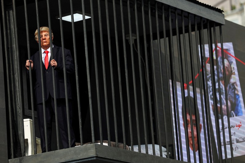 Iran membuat sindiran atau olok-olok terbaru terhadap Presiden Amerika Serikat (AS) Donald Trump, Rabu (21/10/2026). Iran membuat sosok tiruan Trump berada di balik jeruji besi yang dibuat di atas papan reklame. (via REUTERS/Majid Asgaripour)