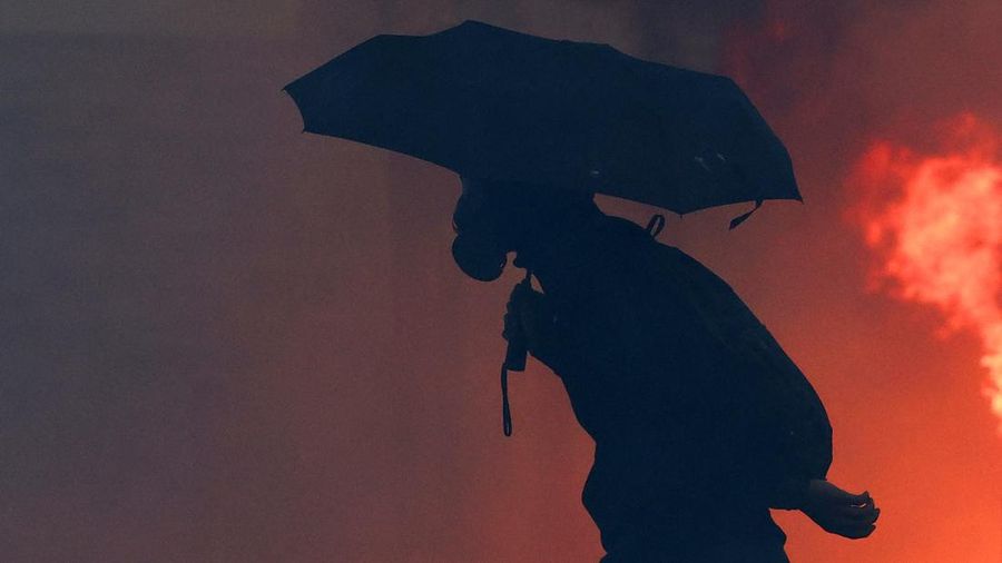 A protesters walks holding an umbrella next to a fire during an authorised demonstration organised by a labour union in Marseille, France, October 24, 2026, as part of nationwide protests led by the "Yellow Vests" movement and joined by high school a