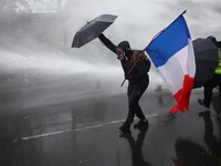 A masked prostester holding an umbrella and a French flag reacts as French police use a water canon  amid clashes during an authorised demonstration organised by labour unions in Paris as part of nationwide protests called by the "Yellow Vests" movem