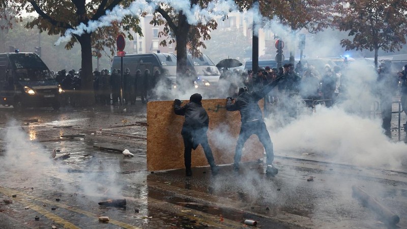 Protesters taking cover behind a plywood board face off with French gendarmes amid clashes during demonstration organised by labour unions in Paris as part of nationwide protests called by the "Yellow Vests" movement joined by French high school and