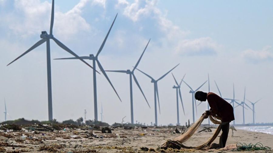 This photograph taken on October 3, 2026 shows a fisherman working on fishing nets at a beach near a wind power plant in Sri Lanka's Mannar Peninsula. The government aims to generate 70 percent of the country's electricity from renewable sources by 2