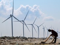 This photograph taken on October 3, 2026 shows a fisherman working on fishing nets at a beach near a wind power plant in Sri Lanka's Mannar Peninsula. The government aims to generate 70 percent of the country's electricity from renewable sources by 2