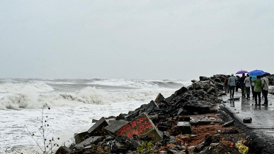Orang-orang membawa payung di sepanjang pesisir Teluk Benggala saat hujan turun di Kakinada, Andhra Pradesh, pada 27 Oktober 2026, menjelang perkiraan kedatangan siklon Arnab ke daratan.