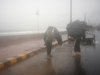 Para wanita berlindung di bawah payung saat air pasang terjadi di tengah hujan dan angin kencang seiring mendekatnya Siklon Arnab, di Visakhapatnam, Andhra Pradesh, India, 27 Oktober 2026. (REUTERS/Ahamad Shaik)