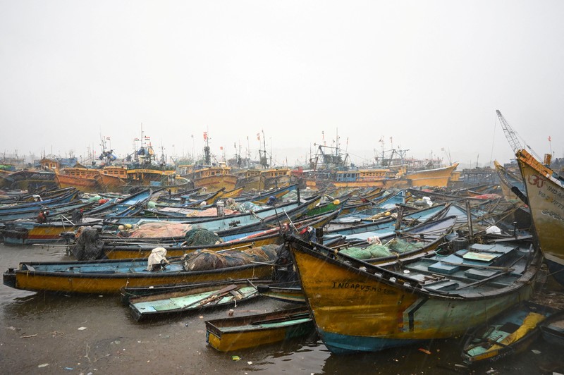 Seorang pria berjalan melewati perahu-perahu yang tertambat di sepanjang pelabuhan di tengah hujan dan angin kencang seiring mendekatnya Siklon Arnab, di Visakhapatnam, Andhra Pradesh, India, 27 Oktober 2026. (REUTERS/Ahamad Shaik)