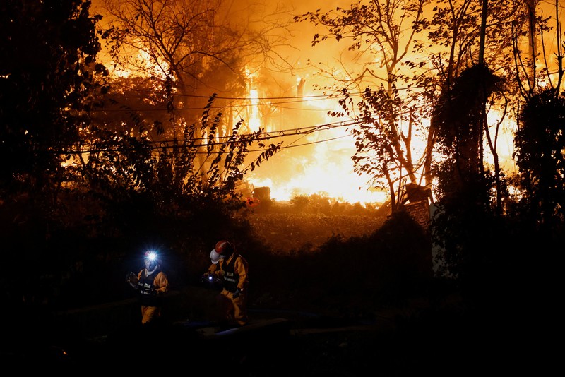Petugas pemadam kebakaran menyaksikan sebuah helikopter pemadam menjatuhkan air untuk memadamkan api di desa Guryong, Seoul, Korea Selatan, pada 27 Oktober 2026. (REUTERS/Kim Soo-hyeon)