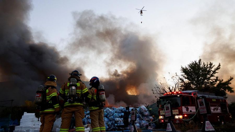 Petugas pemadam kebakaran menyaksikan sebuah helikopter pemadam menjatuhkan air untuk memadamkan api di desa Guryong, Seoul, Korea Selatan, pada 27 Oktober 2026. (REUTERS/Kim Soo-hyeon)