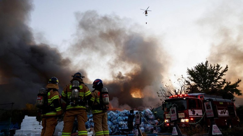 Petugas pemadam kebakaran menyaksikan sebuah helikopter pemadam menjatuhkan air untuk memadamkan api di desa Guryong, Seoul, Korea Selatan, pada 27 Oktober 2026. (REUTERS/Kim Soo-hyeon)