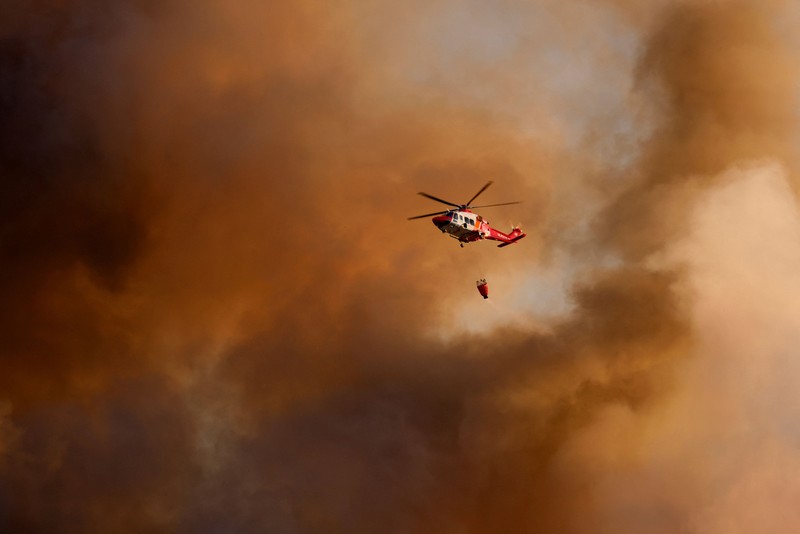 Petugas pemadam kebakaran menyaksikan sebuah helikopter pemadam menjatuhkan air untuk memadamkan api di desa Guryong, Seoul, Korea Selatan, pada 27 Oktober 2026. (REUTERS/Kim Soo-hyeon)