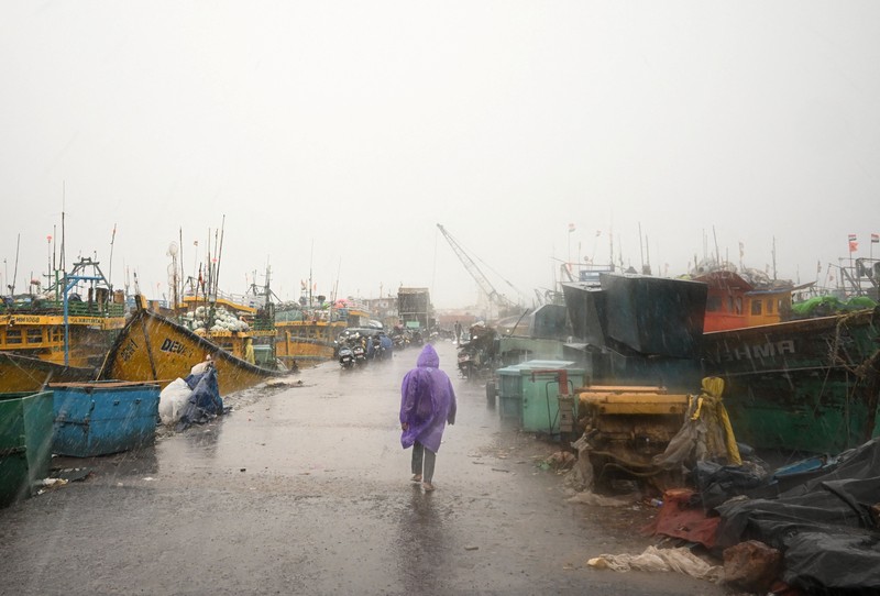 Seorang pria berjalan melewati perahu-perahu yang tertambat di sepanjang pelabuhan di tengah hujan dan angin kencang seiring mendekatnya Siklon Arnab, di Visakhapatnam, Andhra Pradesh, India, 27 Oktober 2026. (REUTERS/Ahamad Shaik)