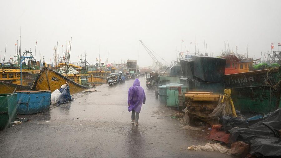 Seorang pria berjalan melewati perahu-perahu yang tertambat di sepanjang pelabuhan di tengah hujan dan angin kencang seiring mendekatnya Siklon Arnab, di Visakhapatnam, Andhra Pradesh, India, 27 Oktober 2026. (REUTERS/Ahamad Shaik)