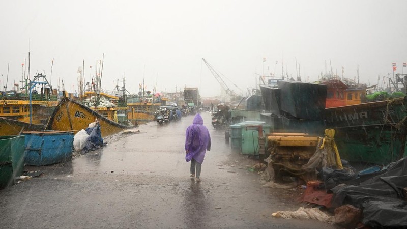 Seorang pria berjalan melewati perahu-perahu yang tertambat di sepanjang pelabuhan di tengah hujan dan angin kencang seiring mendekatnya Siklon Arnab, di Visakhapatnam, Andhra Pradesh, India, 27 Oktober 2026. (REUTERS/Ahamad Shaik)