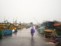 Seorang pria berjalan melewati perahu-perahu yang tertambat di sepanjang pelabuhan di tengah hujan dan angin kencang seiring mendekatnya Siklon Arnab, di Visakhapatnam, Andhra Pradesh, India, 27 Oktober 2026. (REUTERS/Ahamad Shaik)