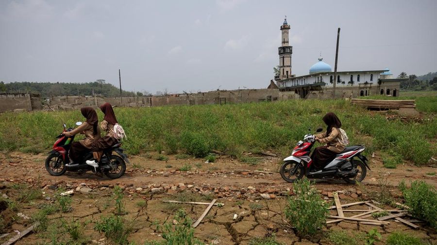 Para pelajar mengendarai sepeda motor melintasi tanah retak di dekat sisa-sisa rumah dan Masjid Al Mujahidin di Desa Somang, yang kembali muncul ke permukaan setelah permukaan air di Waduk Karian—sumber pasokan air bagi wilayah sekitarnya, termasuk Jakarta—menurun akibat kekeringan berkepanjangan yang dipicu oleh fenomena El Niño, di Lebak, Provinsi Banten, Indonesia, 23 Oktober 2026.