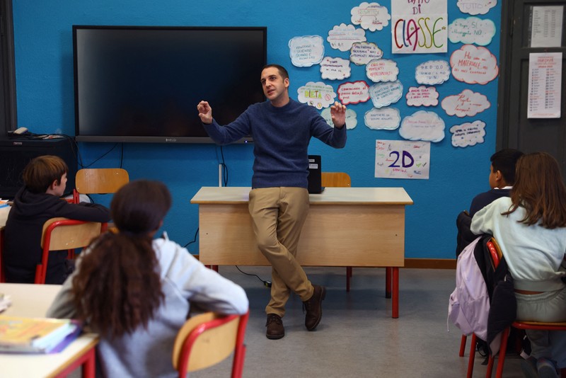 Seorang siswi mengangkat tangannya sementara Giovanni Pavese, guru musik, memperhatikan selama pelajaran di sebuah ruang kelas di sekolah komprehensif negeri 'Simona Giorgi', di Milan, Italia, 23 Oktober 2026. (REUTERS/Claudia Greco)