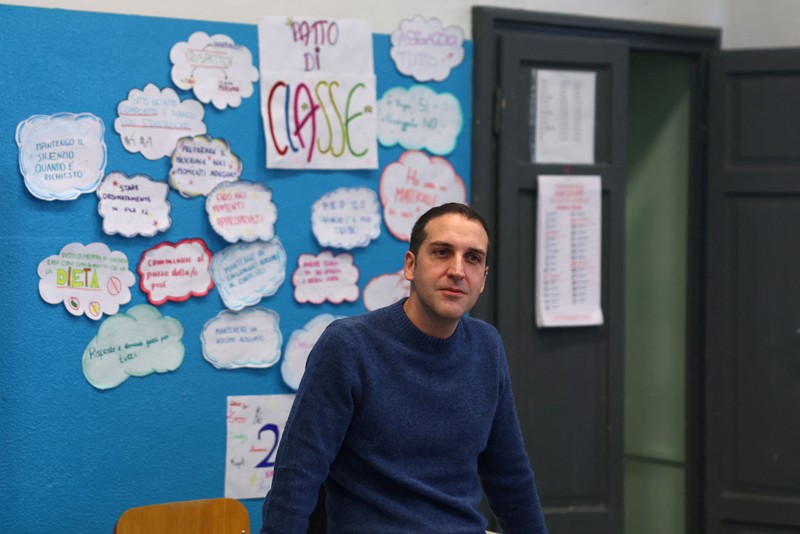 Seorang siswi mengangkat tangannya sementara Giovanni Pavese, guru musik, memperhatikan selama pelajaran di sebuah ruang kelas di sekolah komprehensif negeri 'Simona Giorgi', di Milan, Italia, 23 Oktober 2026. (REUTERS/Claudia Greco)
