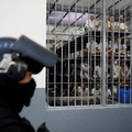 Seorang petugas kepolisian berdiri sementara para narapidana memperhatikan dari dalam sel, dalam kunjungan Menteri Kehakiman dan Keamanan Publik El Salvador, Gustavo Villatoro, dan Presiden Peru, Keiko Fujimori (tidak tampak dalam foto), ke Pusat Pen
