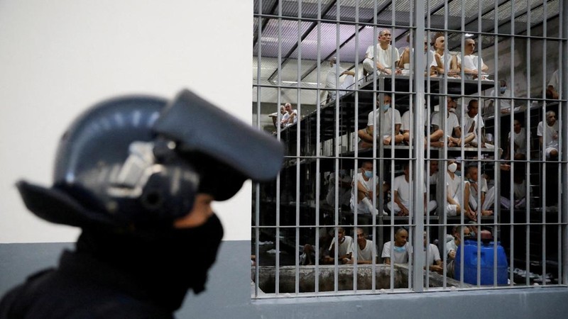 Seorang petugas kepolisian berdiri sementara para narapidana memperhatikan dari dalam sel, dalam kunjungan Menteri Kehakiman dan Keamanan Publik El Salvador, Gustavo Villatoro, dan Presiden Peru, Keiko Fujimori (tidak tampak dalam foto), ke Pusat Penahanan Terorisme (CECOT) di Tecoluca, El Salvador, pada 29 Oktober 2026.