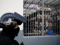 Seorang petugas kepolisian berdiri sementara para narapidana memperhatikan dari dalam sel, dalam kunjungan Menteri Kehakiman dan Keamanan Publik El Salvador, Gustavo Villatoro, dan Presiden Peru, Keiko Fujimori (tidak tampak dalam foto), ke Pusat Pen