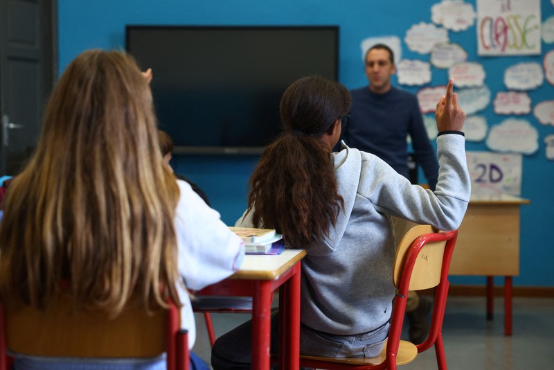 Seorang siswi mengangkat tangannya sementara Giovanni Pavese, guru musik, memperhatikan selama pelajaran di sebuah ruang kelas di sekolah komprehensif negeri 'Simona Giorgi', di Milan, Italia, 23 Oktober 2026. (REUTERS/Claudia Greco)