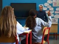Seorang siswi mengangkat tangannya sementara Giovanni Pavese, guru musik, memperhatikan selama pelajaran di sebuah ruang kelas di sekolah komprehensif negeri 'Simona Giorgi', di Milan, Italia, 23 Oktober 2026. (REUTERS/Claudia Greco)